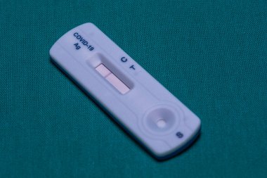 Bir COVID-19 antijen test kasetinin yakın çekiminde tek bir kontrol hattı görüntülenir, bu da deniz mavisi arka planında negatif bir sonucu gösterir..