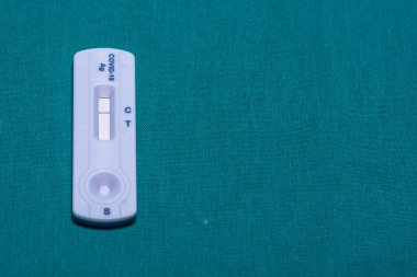 Close-up of a COVID-19 antigen rapid test cassette displaying two lines (control and test), confirming a positive result, placed on a teal background. clipart