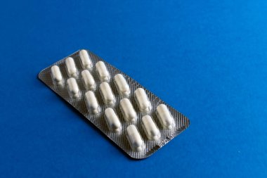 Katı mavi arka plana yerleştirilmiş beyaz kapsüller içeren gümüş su toplayıcılarının yakın plan görüntüsü.