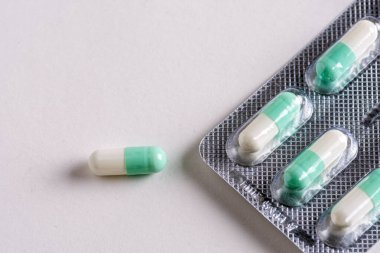 Benzer kapsüllerin bulunduğu su toplayan bir paketin yanına yerleştirilmiş yeşil ve beyaz bir kapsülün makro görüntüsü. Tarafsız arkaplan.