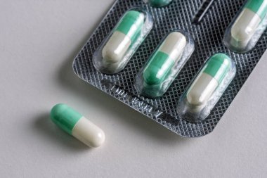 Beyaz bir yüzeyde yeşil ve beyaz bir ilaç kapsülünün yakın plan çekimleri, arka planda bulanık su toplamaları, sağlık hizmetleri ve ilaçların