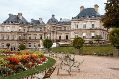 The Luxembourg Palace in Paris surrounded by vibrant flowerbeds, manicured greenery, and iconic garden chairs on a cloudy day. clipart