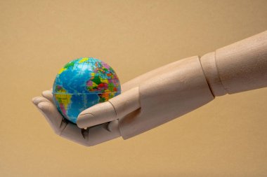 Daha iyi bir gelecek için çevresel koruma, küresel sorumluluk ve sürdürülebilir uygulamaları sembolize eden küçük bir küreyi tutan ahşap eklemli el.