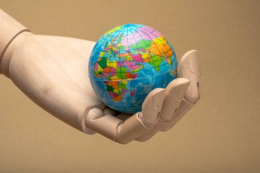 Tahta eklemli el, küçük bir küreyi görünür kıtalar ve meridyenlerle tutuyor, seyahat, sürdürülebilirlik ve uluslararası işbirliği gibi küresel kavramları temsil ediyor.
