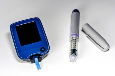 Bir test şeridi ve beyaz bir yüzey üzerinde dinlenen insülin kaleminin yer aldığı glikoz ölçer, diyabet yönetimi ve sağlık uygulamalarının temel yönlerini göstermektedir.