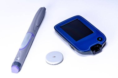 İnsülin kalem, devamlı glikoz monitörü ve temiz beyaz bir yüzeye yerleştirilmiş sensör diyabet yönetiminin temel unsurlarını ve etkili kan şekeri kontrolünü gösteriyor.