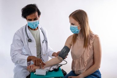 Yüz maskesi takan doktor, doktor muayenesinde koruyucu maske takan kadın hastanın kan basıncını ölçüyor.