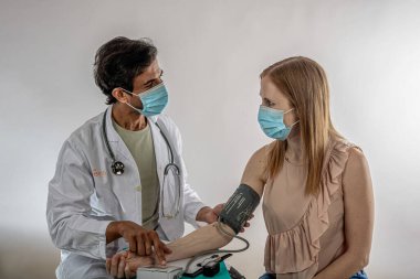 Doktor, her ikisi de koruyucu yüz maskesi takan kadın hastaların tansiyonlarını ölçerek, sağlık önlemlerini ve salgın hastalıklar bağlamında sağlık hizmetlerini vurguladı.