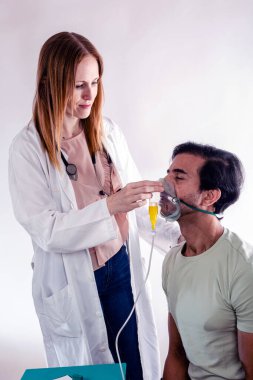 Laboratuvar önlüğü giyen kadın doktor ve steteskop, erkek hastaların yüzüne dikkatlice oksijen maskesi takıyor ve klinik bir ortamda solunum desteği uyguluyor.