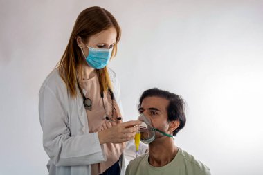 Cerrahi maske takan ve steteskop kullanan kadın doktor hastane odasında erkek hastaya oksijen maskesi takıyor, tıbbi tedavi sırasında solunum desteği sağlıyor.