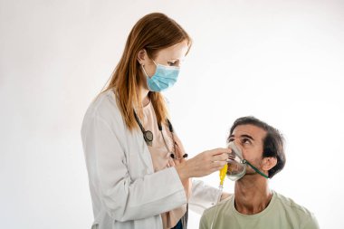 Cerrahi maske takan kadın doktor ve steteskop beyaz arkaplan ile hastane odasında muayene sırasında erkek hastaya oksijen maskesi takıyor.