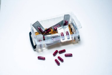 Beyaz arka planda saydam plastik bir kutudan birkaç kırmızı hap ve su toplayıcısı dökülüyor. İlaç, sağlık ve ilaç ile ilgili bir bileşim oluşturuyor.