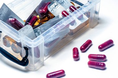 Şeffaf plastik bir kutudan dökülen kırmızı haplar, temiz beyaz arka plana karşı aşırı doz veya yanlış ilaç yönetimi endişelerini vurguluyor