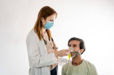 Yüz maskesi takan kadın doktor ve steteskop, erkek hastaların yüzüne dikkatlice oksijen maskesi takıyor ve parlak bir klinik ortamda solunum desteği sağlıyor.