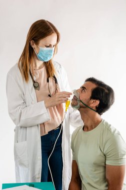 Cerrahi maske takan ve steteskop takan kadın doktor hastane veya klinikteki tıbbi konsültasyon sırasında erkek hastaya oksijen maskesi takıyor ve solunum desteği ve bakım sağlıyor.