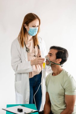 Kadın doktor yüz maskesi takıyor ve erkek hasta için oksijen maskesi tutuyor. Sağlık ortamında tıbbi bir prosedür sırasında, hasta bakımını ve solunum sağlığını destekliyor.