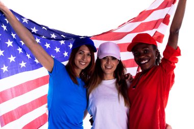 Beyzbol şapkası ve renkli tişörtler giyen üç mutlu kadın, bağımsızlık gününü kutlamak için büyük bir Amerikan bayrağı tutuyorlar. Vatanseverlik kavramı, bağımsızlık günü