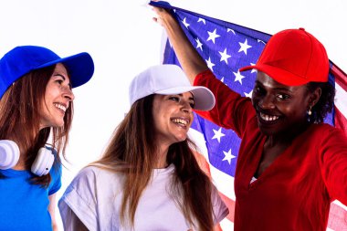 Beyzbol şapkası takan ve elinde Birleşik Devletler bayrağı olan üç heyecanlı kadın destekçi, 4 Temmuz 'u neşe ve vatanseverlikle kutluyorlar. Vatanseverlik kavramı, bağımsızlık günü