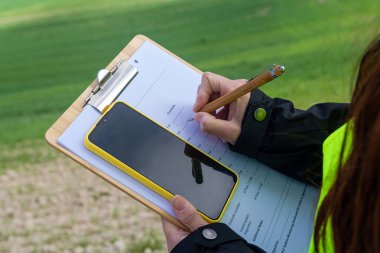 Tarım mühendisi panoya notlar yazıyor ve buğday tarlasında cep telefonu kullanıyor, bitkilerle ilgileniyor ve hasat hazırlıyor.