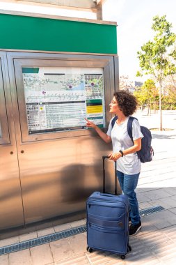 Sırt çantalı ve tramvay çantalı kadın dijital göçebe şehirde bir sonraki hamlesini planlarken ve seyahat ederken bir toplu taşıma haritasını işaret ediyor.