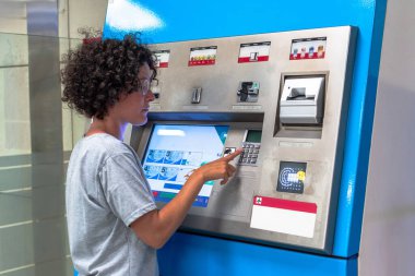 Gideceği yeri dijital dokunmatik ekrandan seçen genç bir kadın bir sonraki seyahat macerası için tren bileti alıyor.