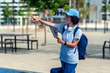 Kadın turist, şehir merkezinde bir haritayı tutarken, elinde kulaklık ve sırt çantası olan ve yaz tatili macerasına dalmış bir kadın turist.