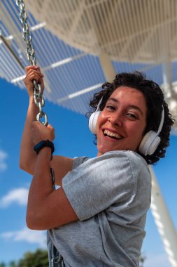 Neşeli dijital göçebe kadın kulaklık takıyor ve elinde sallanan bir zincir tutuyor dışarıda çalışıyor, dijital göçebe yaşam tarzını benimserken özgürlüğünün ve hareketliliğinin tadını çıkarıyor.