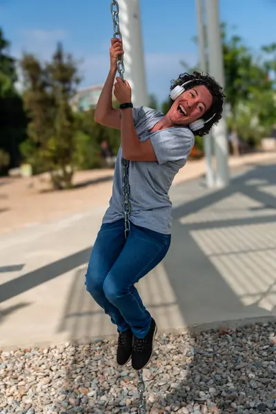 Kulaklıklı neşeli dijital göçebe kadın, modern bir şehir ortamında özgürlüğünün ve iş hayatının dengesinin tadını çıkararak, neşeli bir şekilde zincirden sarkıyor.