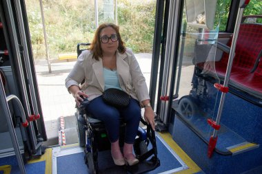 Elektrikli sandalye kullanan bir iş kadını modern bir otobüse giriş rampası ile giriyor ve ulaşılabilir ulaşımı vurguluyor. Katılım kavramı, uyarlanmış toplu taşıma