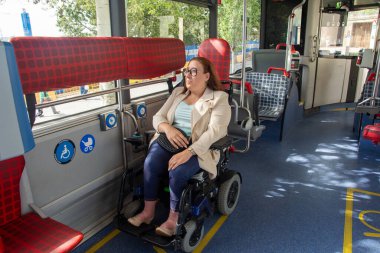Businesswoman sitting on a wheelchair is traveling on a modern bus equipped with dedicated space and enjoying her comfortable ride. Concept of inclusion, adapted public transport