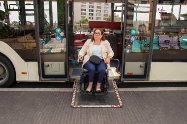 Caucasian middle aged woman using a wheelchair ramp exiting a public transport bus, promoting accessibility and inclusivity in urban transportation. Concept of inclusion, adapted public transport