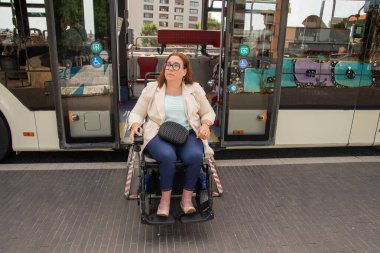 Middle aged woman exiting a public transport bus using a wheelchair ramp, showcasing accessible transportation for disabled individuals. Concept of inclusion, adapted public transport