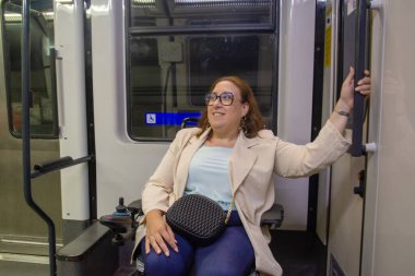 Motorlu tekerlekli sandalye kullanan mutlu iş kadını ulaşılabilir bir toplu taşıma aracıyla seyahat ederken kapı kolunu tutuyor. Katılım kavramı, uyarlanmış toplu taşıma