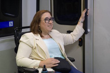 Modern bir metro vagonunun kapısını açarken gülümseyen gözlüklü ve ceketli bir iş kadını, ulaşılabilir toplu taşıma araçlarının altını çiziyor. Katılım kavramı, uyarlanmış toplu taşıma