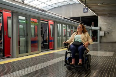 Elektrikli sandalyede ulaşılabilir bir metro istasyonunda bekleyen iş kadını toplu taşımacılığa dahil olmanın altını çiziyor. Katılım kavramı, uyarlanmış toplu taşıma