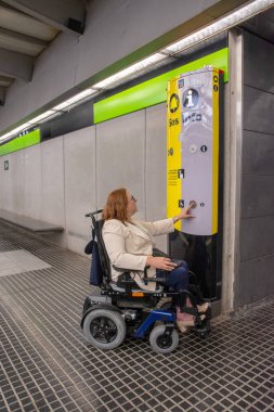 Tekerlekli sandalyedeki iş kadını modern bir metro istasyonunda ulaşılabilir bir bilgi noktasını kullanarak, kapsamlı tasarımın altını çiziyor. Katılım kavramı, uyarlanmış toplu taşıma