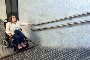 Tekerlekli sandalyesiyle ulaşılabilir bir metro girişinde gezinen iş kadını, kentsel tasarım ihtiyacını vurguluyor. Katılım kavramı, uyarlanmış toplu taşıma