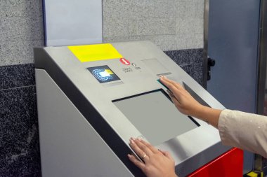 Kadın metro istasyonunda tren bileti almak, dokunmatik ekrana dokunmak ve bağlantısız bir yöntemle ödeme yapmak için self-servis bilet makinesini kullanıyor. Katılım kavramı, uyarlanmış toplu taşıma
