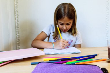 Not defterine renkli kalemlerle resim çizen liseli kız, ödevlerini yapıyor ya da okula hazırlanıyor.