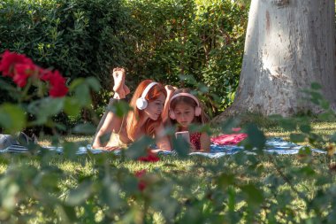 Anne ve kızı parkta bir battaniyeye uzanıp, müzik dinleyip, etrafı doğa ve neşe ile çevrili akıllı bir telefondan videolar izlerken birlikte zaman geçiriyorlar.