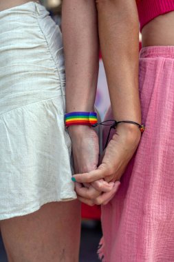 İki kadın el ele tutuşuyor, biri canlı bir gökkuşağı bileziğiyle süslenmiş, aşk ve birlik dolu neşeli bir eşcinsel onur etkinliği sırasında lgbtq 'ı kutluyor ve gurur ve destek veriyor.
