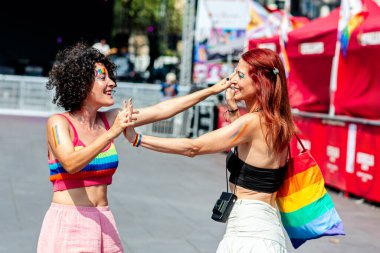 Gurur verici bir olay sırasında iki kadın dans ediyor ve sevgi gösteriyorlar, neşe, kapsama ve lgbtq artı hakları ifade ediyorlar, gökkuşağı bayrakları ve vücut boyaları gururlarını sembolize ediyor.
