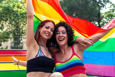 Igbtq artı gurur, çeşitlilik ve açık hava kutlamalarında cinsel ifade özgürlüğünü sembolize eden büyük bir gökkuşağı bayrağı tutan iki neşeli kadın.