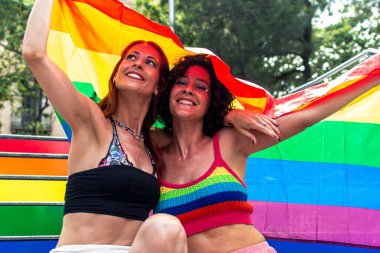 Igbtq artı hakları, aşkı ve topluluktaki çeşitliliğin güzelliğini coşkuyla kutlayan, canlı bir gurur geçidi sırasında büyük bir gökkuşağı bayrağını kucaklayan ve gülümseyen iki kadın.