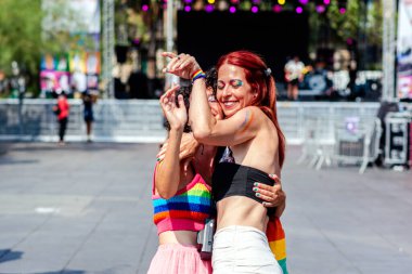 İki kadın bir gurur etkinliğinde sarılıyor ve gülümsüyor, aşkı ifade ediyorlar, kapsayıcılığı ve mutluluğu, gökkuşağı bayrağı ve renkli kıyafetlerle lgbtq 'ı sembolize ediyorlar artı gurur ve kutlamaları.