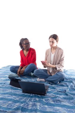 İki kadın bir battaniyenin üzerinde bacak bacak üstüne atmış, dizüstü bilgisayarla ve akıllı telefonla uğraşıyorlar, bir projede işbirliği yapıyorlar ve aynı zamanda uzaktan kumandalı çalışmanın ve modern teknolojinin keyfini çıkarıyorlar.