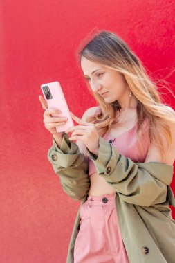 Modayı takip eden genç kadın, dijital dünyada canlı kırmızı bir zemin üzerinde gezinerek teknoloji ve iletişim ile bağlantılı modern yaşam tarzını gözler önüne seriyor.