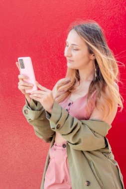 Çevrimiçi alışveriş, sosyal medya ve mobil bankacılık için akıllı telefon uygulaması kullanan turistler, canlı kırmızı duvara karşı durarak sonbahar seyahatlerinin keyfini çıkarıyorlar.