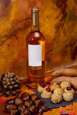 Boş etiketli şarap şişesi, kestane, kavrulmuş tatlı patates, kozalak, panelletler ve kuru sonbahar yaprakları Castanyada 'nın katalan geleneğini kutlayan sıcacık bir sonbahar yaşamı yaratıyor.