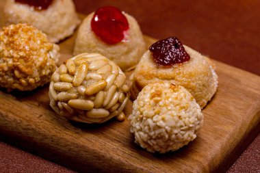 Panelletler olarak bilinen küçük, yuvarlak tatlılar, çam fıstığı, şekerli meyve ve susam tohumlarıyla süslenmiş, ahşap bir tahtanın üzerinde dinleniyor, Castanyada 'nın katalan kutlamalarında eğlenmeye hazır.